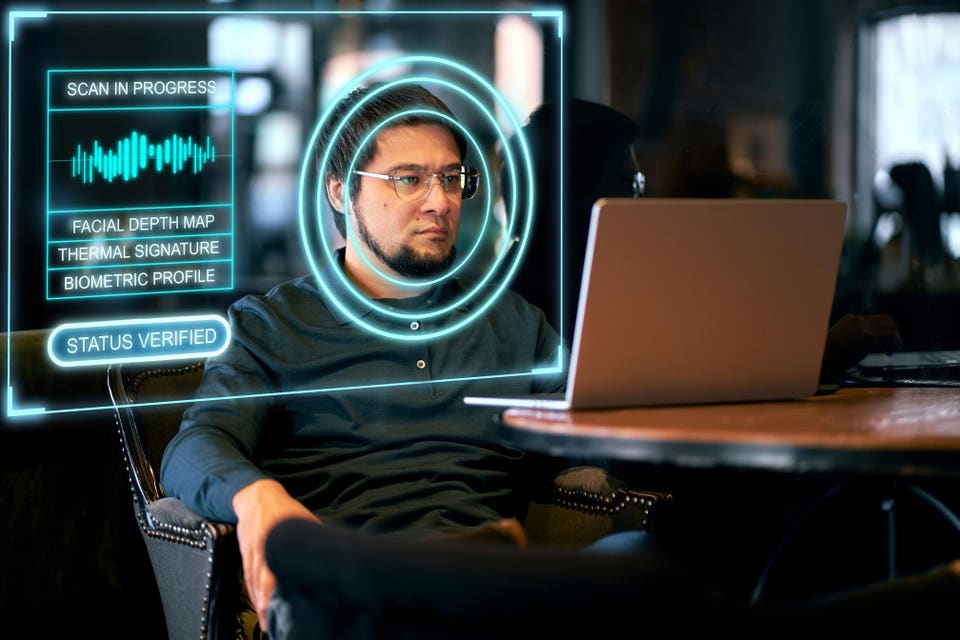 A professional man on a laptop undergoing facial biometric verification, as part of the identity verification process